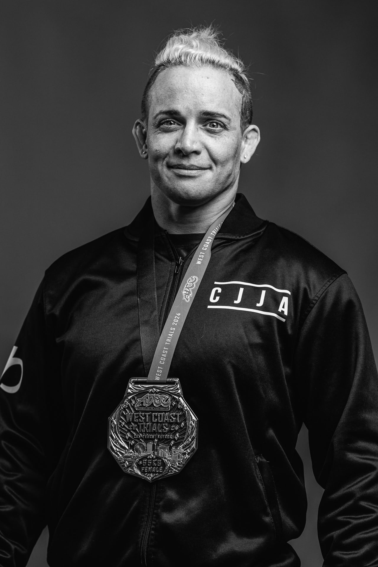 Dr. Jen Case in a Charlotte Jiu-Jitsu Academy jacket, black and white portrait with a West Coast Trials medal.