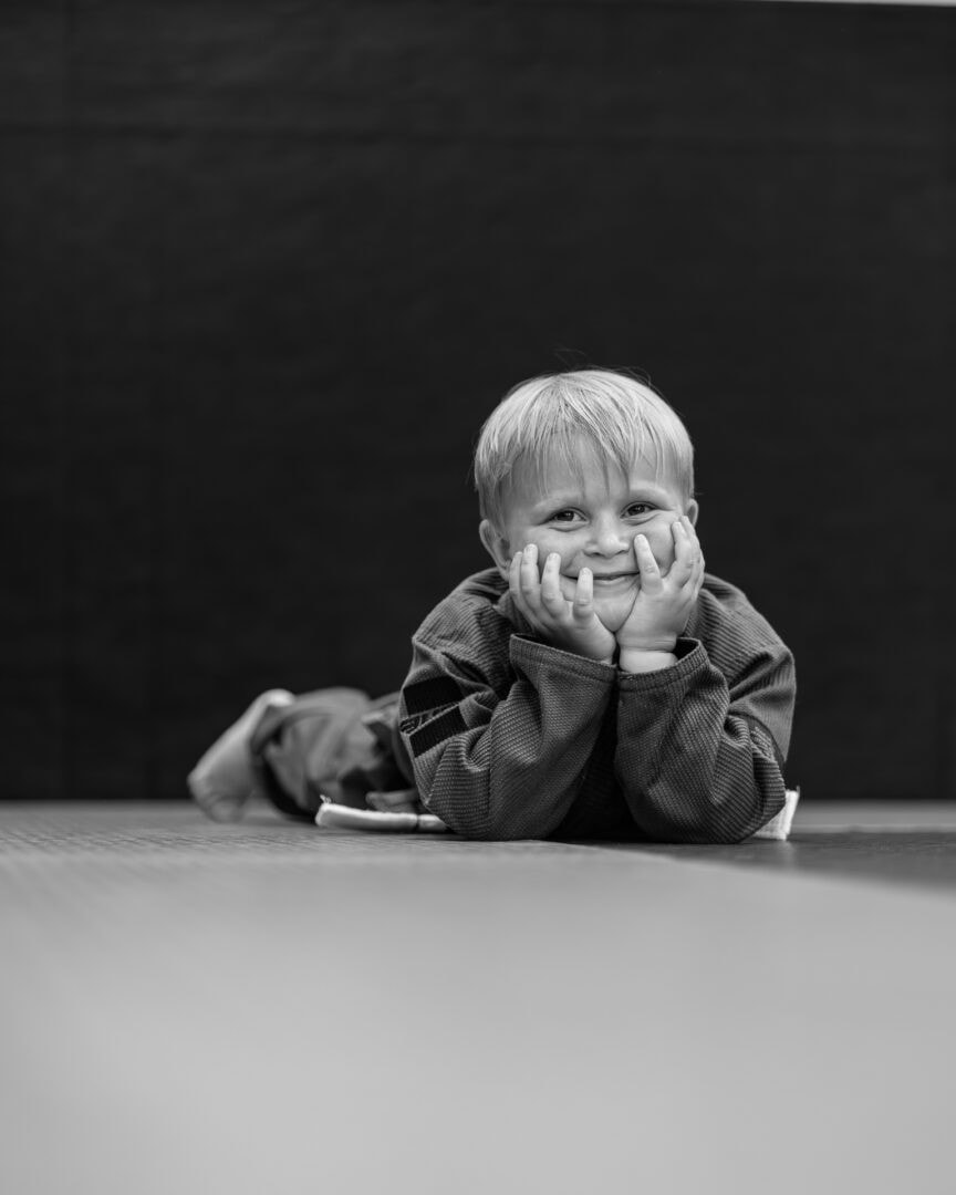 Young child lying on stomach on the mat with hands on cheeks, smiling.