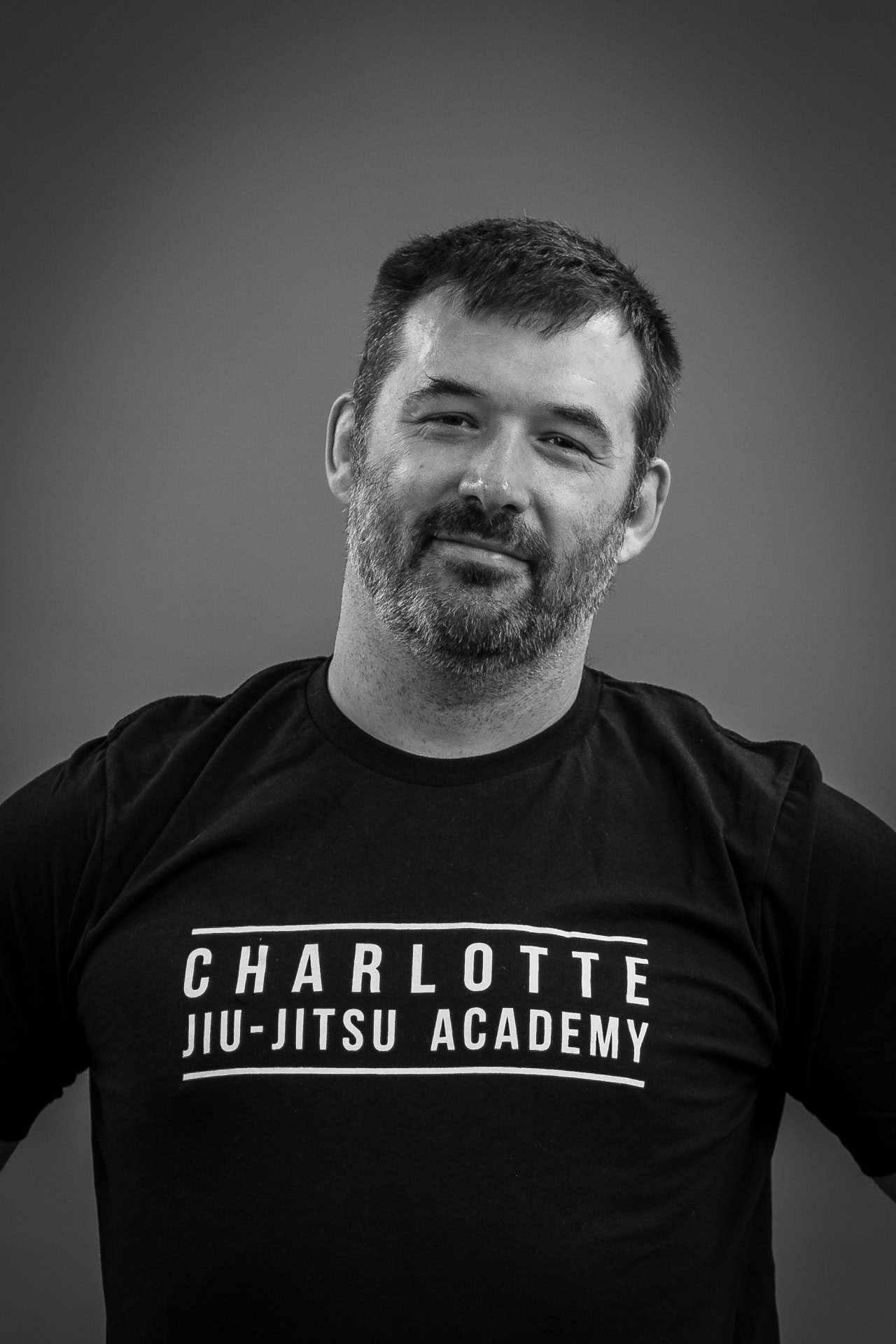 Black and white portrait of a man wearing a Charlotte Jiu-Jitsu Academy t-shirt.
