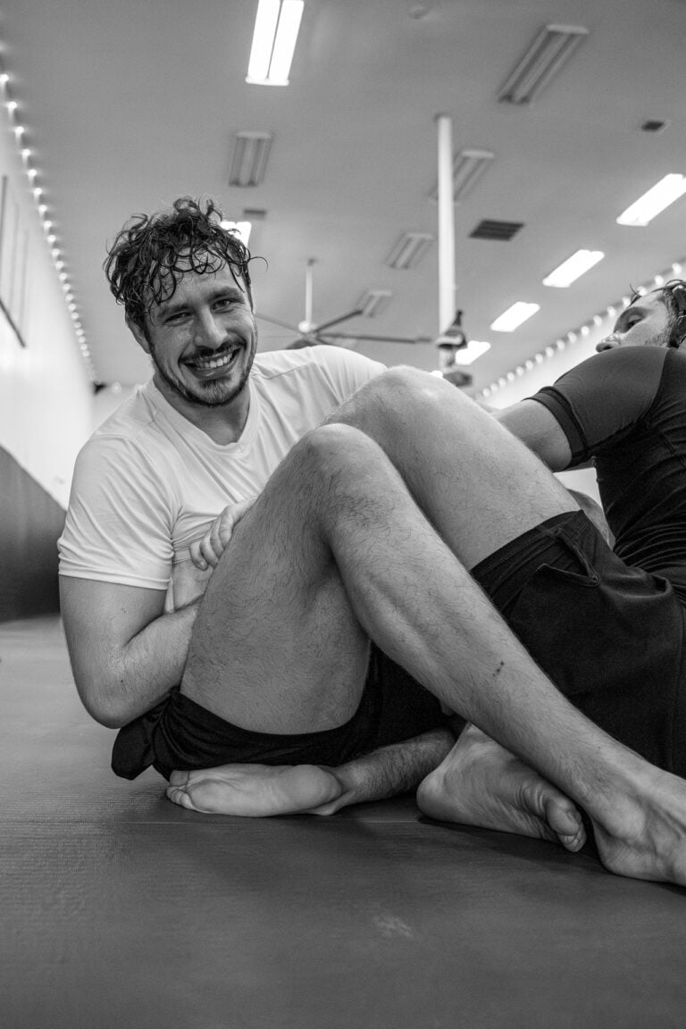 Two men practicing grappling on a padded mat in a well-lit indoor training gym.