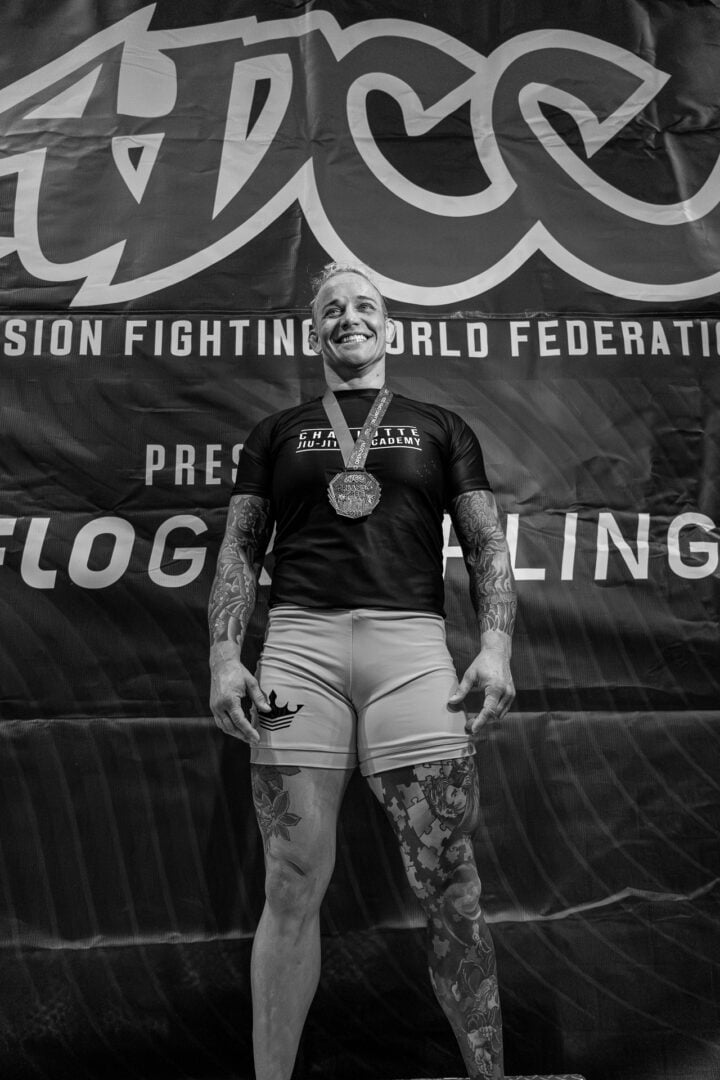 Athlete with tattoos stands on podium wearing medal, shorts, and a t-shirt at competition.