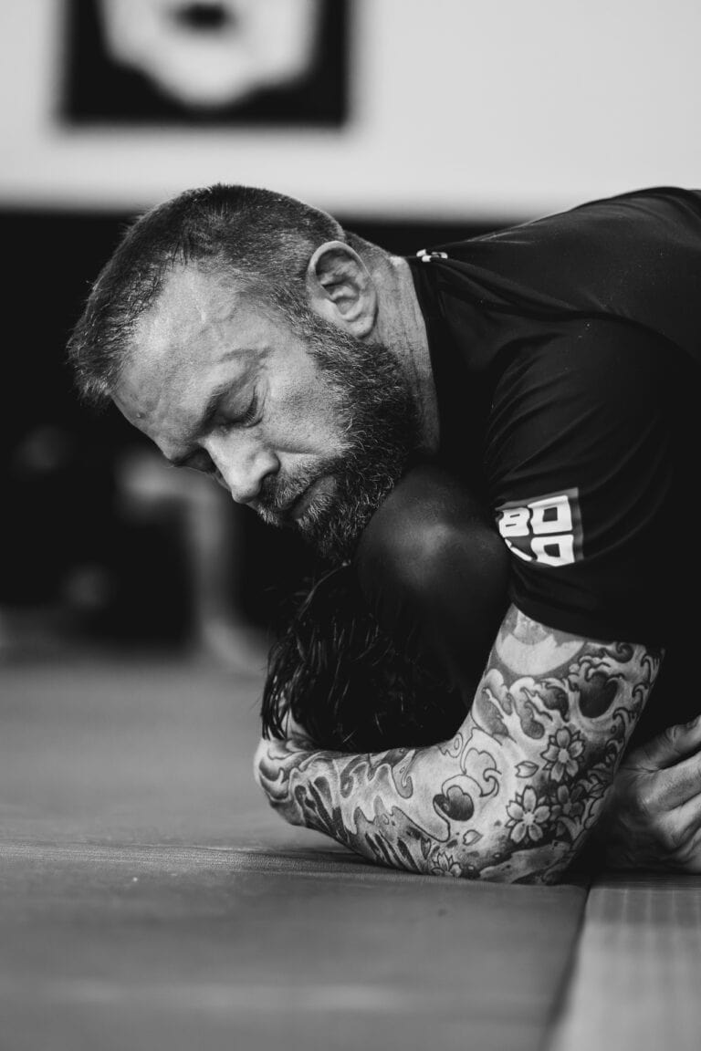 close-up black and white image of a tattooed man grappling during a wrestling match on a mat